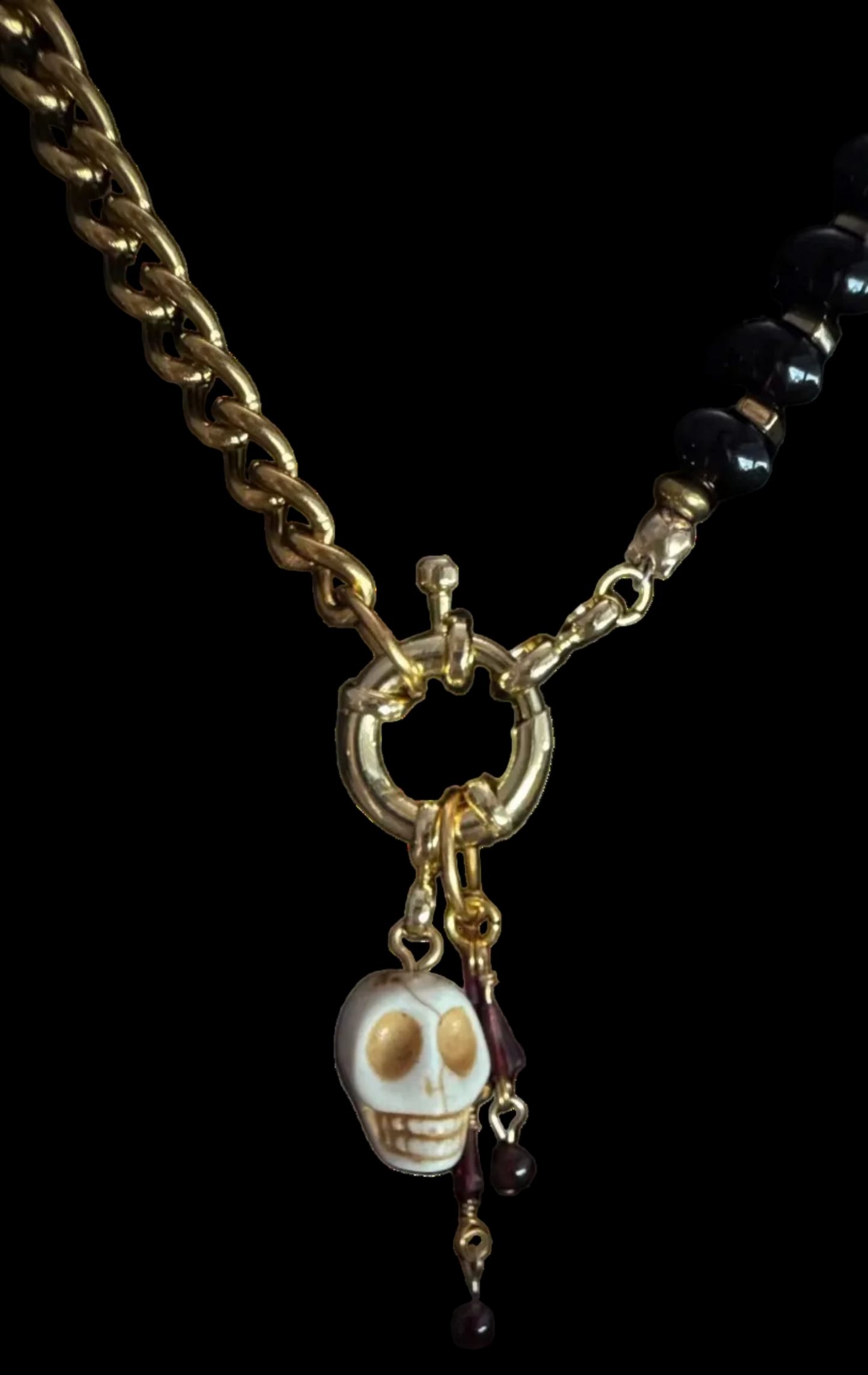 A gothic-style necklace featuring a chunky gold chain, black faceted beads, a gold ring clasp, and a dangling skull charm with dark beads.