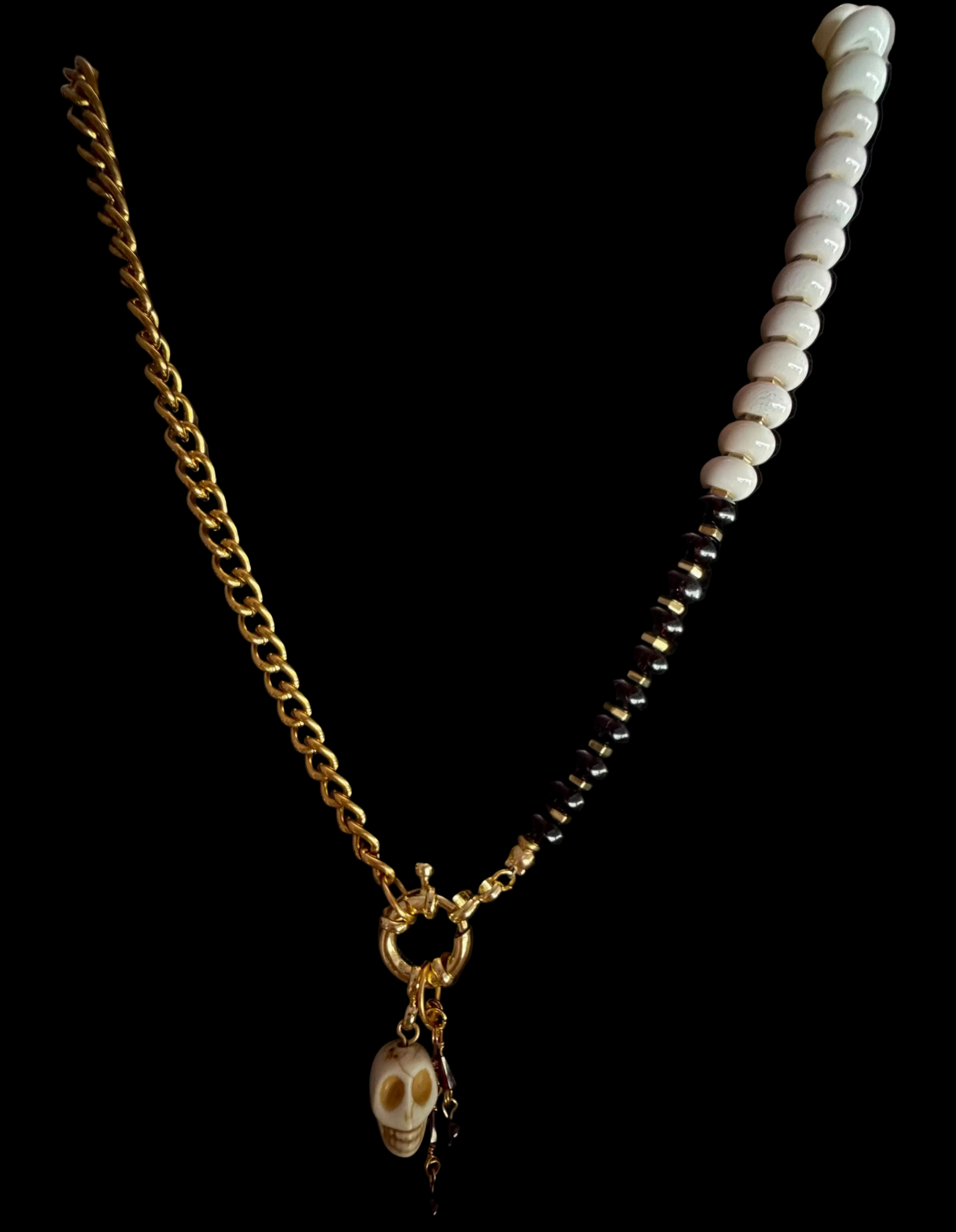 A gold chain necklace displayed on a black jewelry bust, featuring a skull pendant and a section of black and white beads on one side, with waterproof curs chair on the other